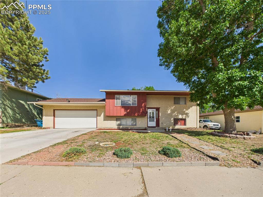Caption: View of front of property with brick siding, an attached garage, and driveway