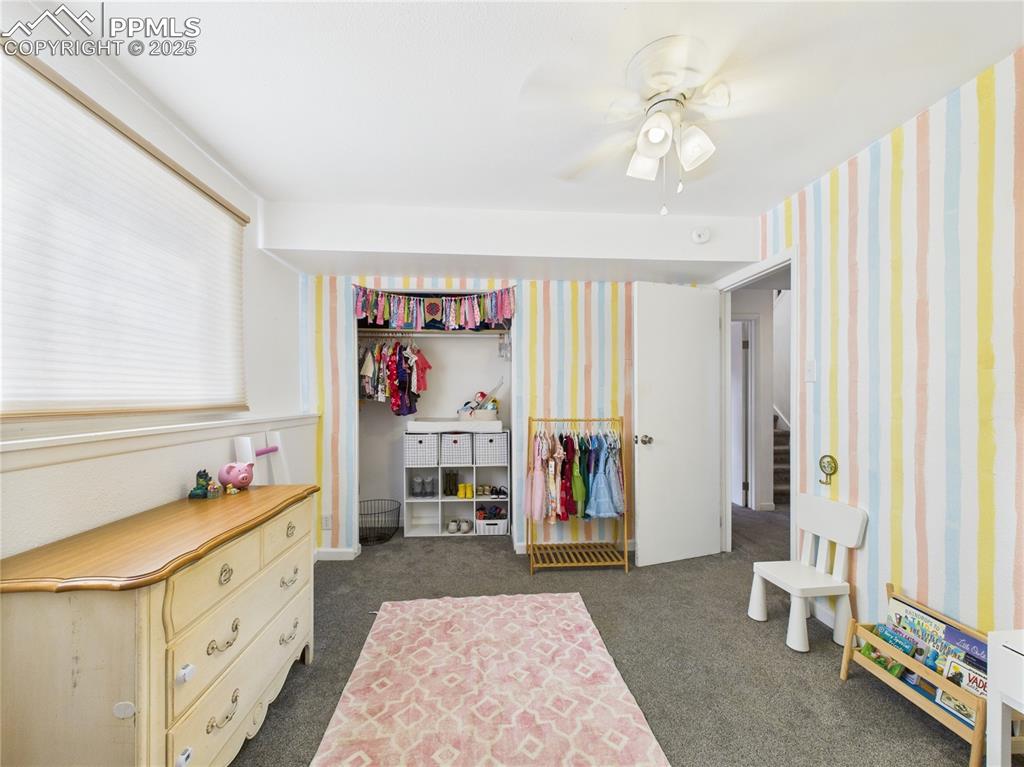 Image 26 of 41: Bedroom with dark colored carpet, wallpapered walls, and a ceiling fan