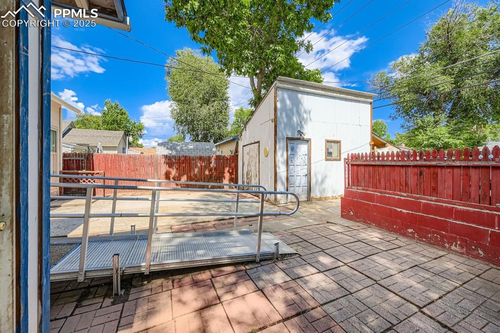 Image 26 of 28: Fenced backyard with an outbuilding and a patio