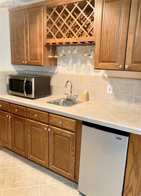 Image 23 of 33: The basement wet bar boasts a tiled countertop & backsplash, wine rack and