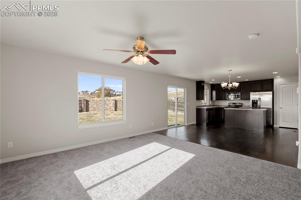 Image 4 of 35: Unfurnished living room with a chandelier, a ceiling fan, dark carpet, and 