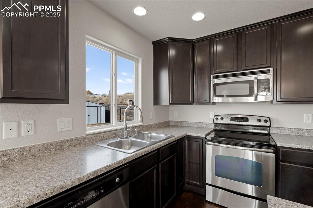 Image 7 of 35: Kitchen with stainless steel appliances, dark brown cabinets, light counter