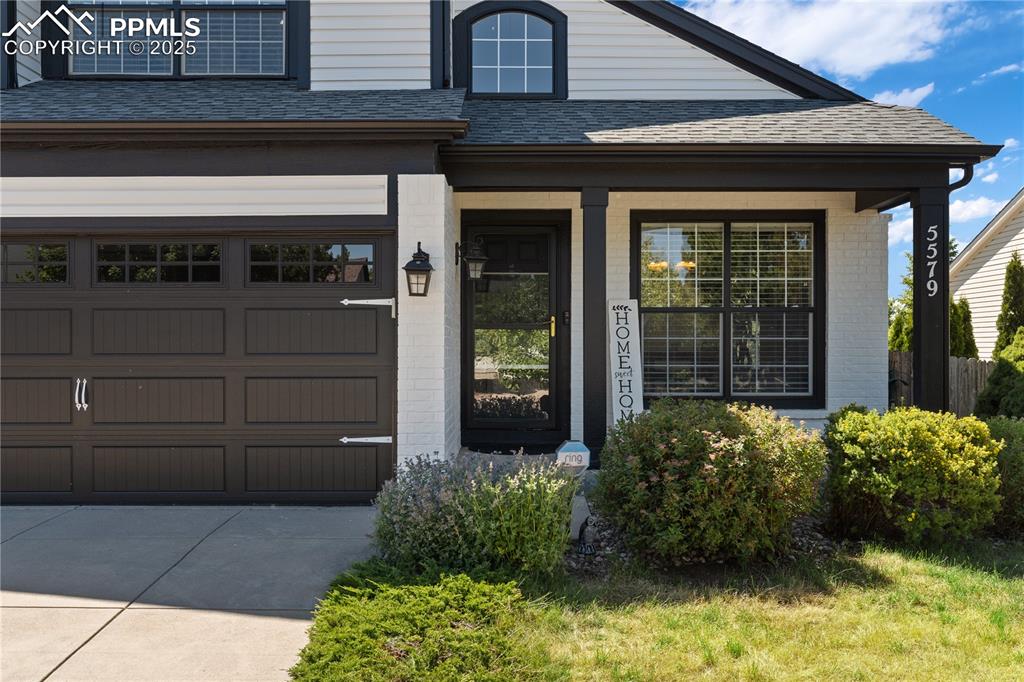 Image 2 of 31: Doorway to property with brick siding, driveway, an attached garage, roof w