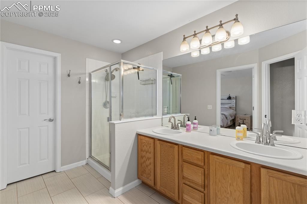 Image 26 of 31: Bathroom with connected bathroom, a shower stall, double vanity, and tile p