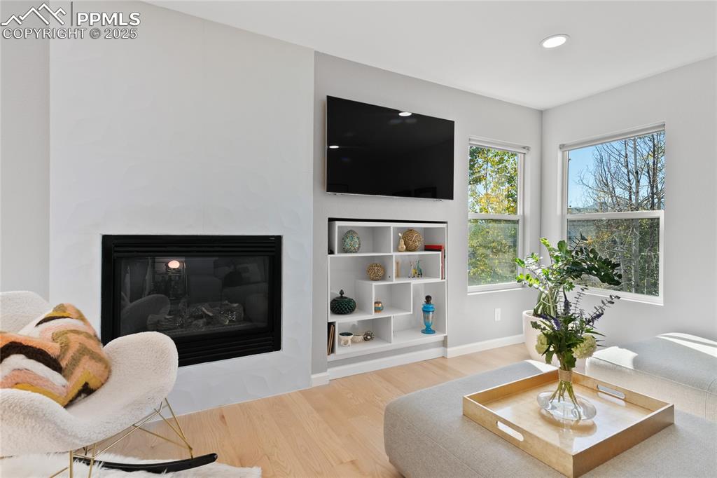 Image 12 of 47: Living area with a glass covered fireplace, light wood-style floors, and re