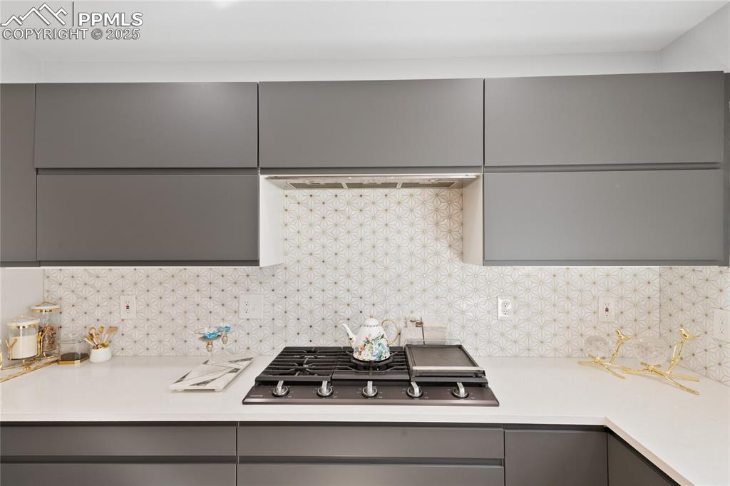 Image 16 of 47: Kitchen with gray cabinetry, backsplash, black gas cooktop, modern cabinets