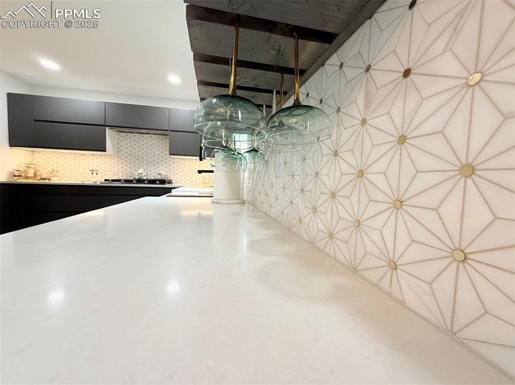 Image 18 of 47: Kitchen with dark cabinets, tasteful backsplash, light stone countertops, a