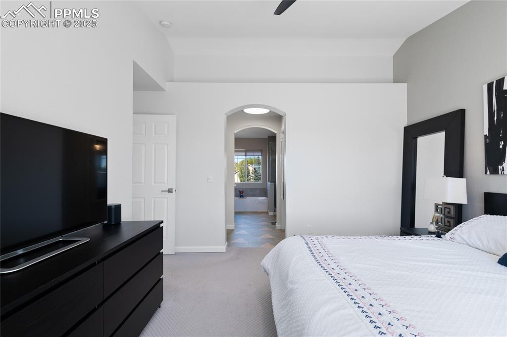 Image 31 of 47: Bedroom with arched walkways, light carpet, ensuite bath, and a ceiling fan