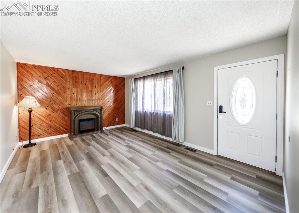 Image 10 of 48: Unfurnished living room with wooden walls, a textured ceiling, light wood-s