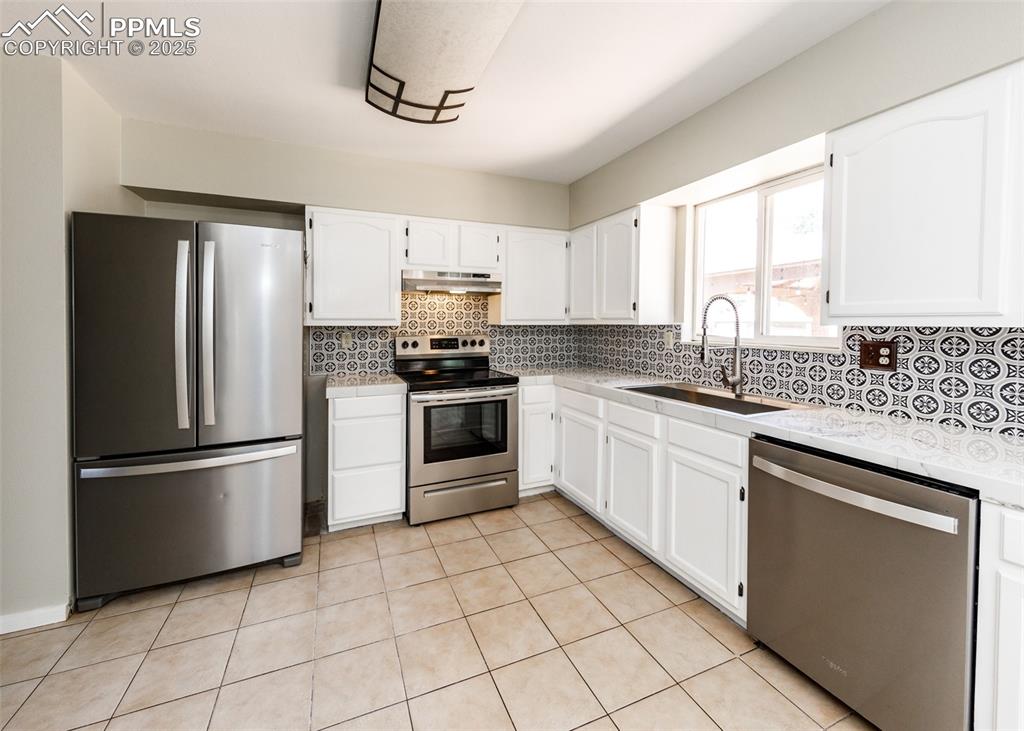 Image 12 of 48: Kitchen with stainless steel appliances, white cabinetry, tasteful backspla