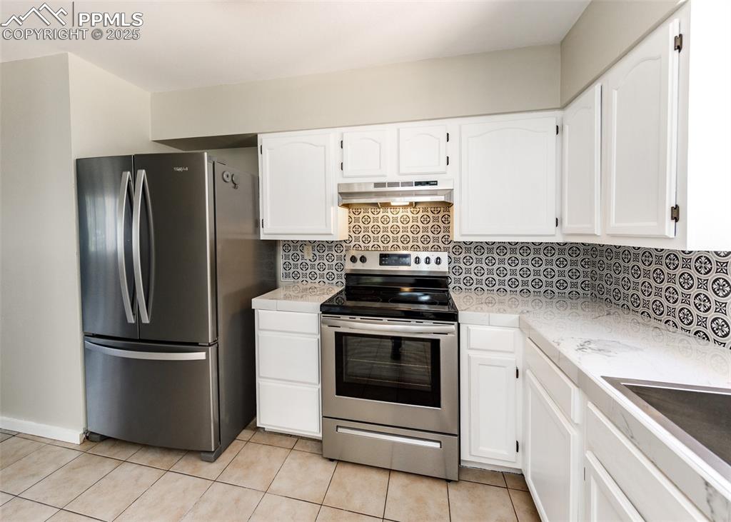 Image 15 of 48: Kitchen with decorative backsplash, stainless steel appliances, white cabin