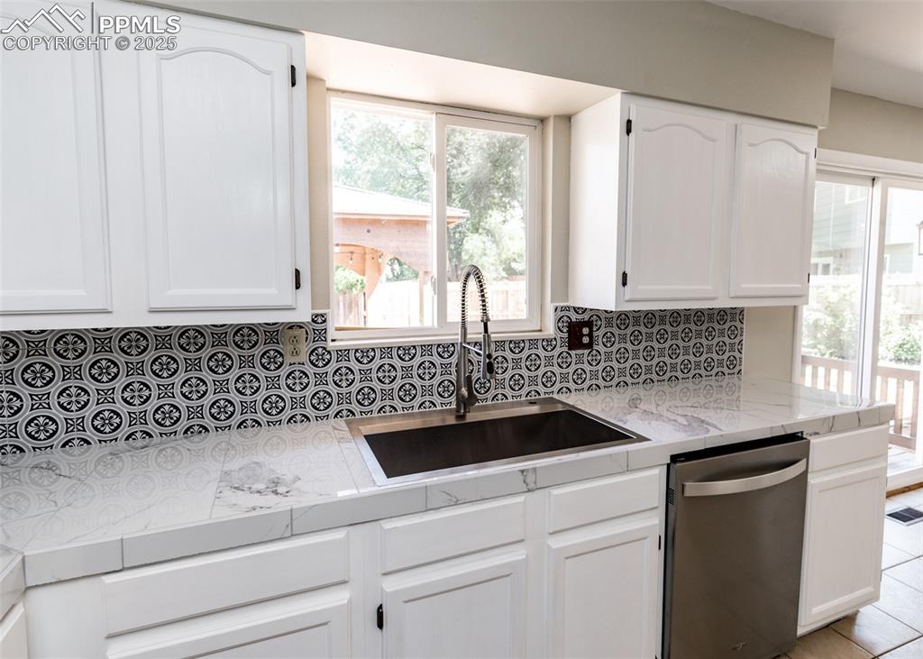 Image 16 of 48: Kitchen featuring white cabinets, dishwasher, healthy amount of natural lig