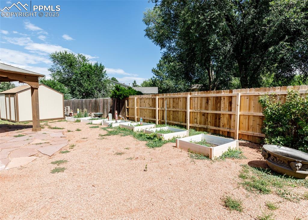 Image 47 of 48: Fenced backyard with a storage unit, a patio, a vegetable garden, and a gaz