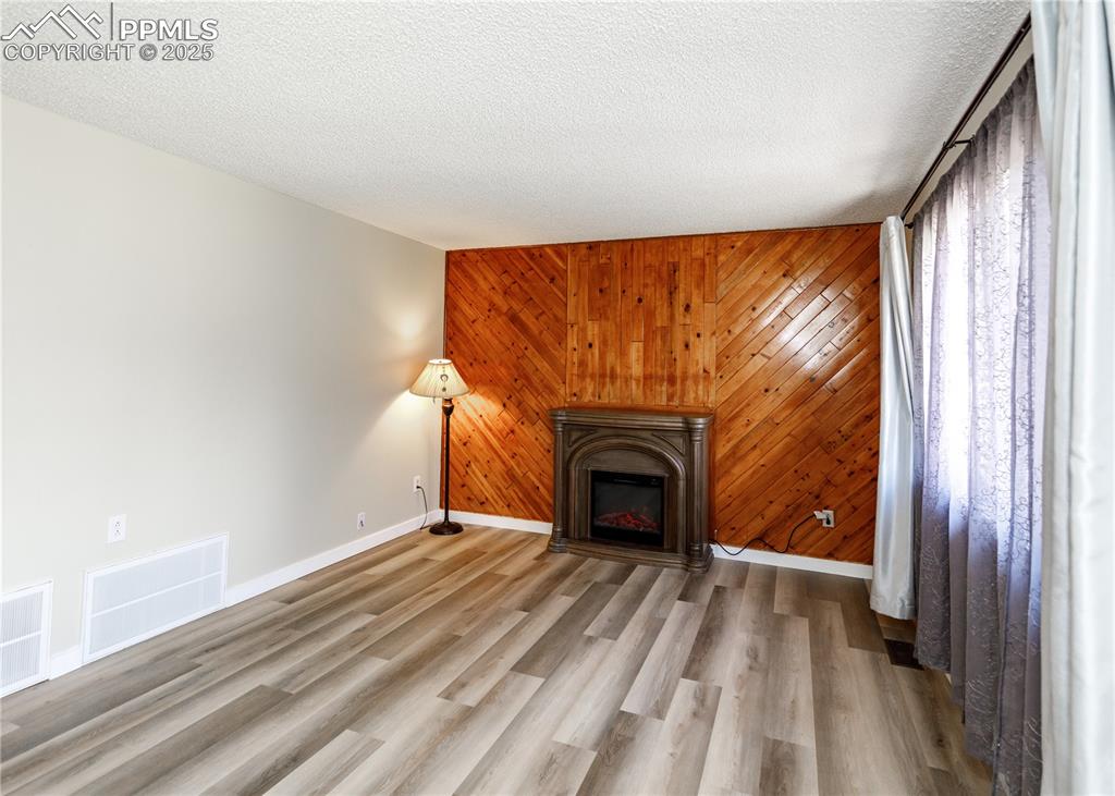 Image 8 of 48: Unfurnished living room with wooden walls, a glass covered fireplace, wood 