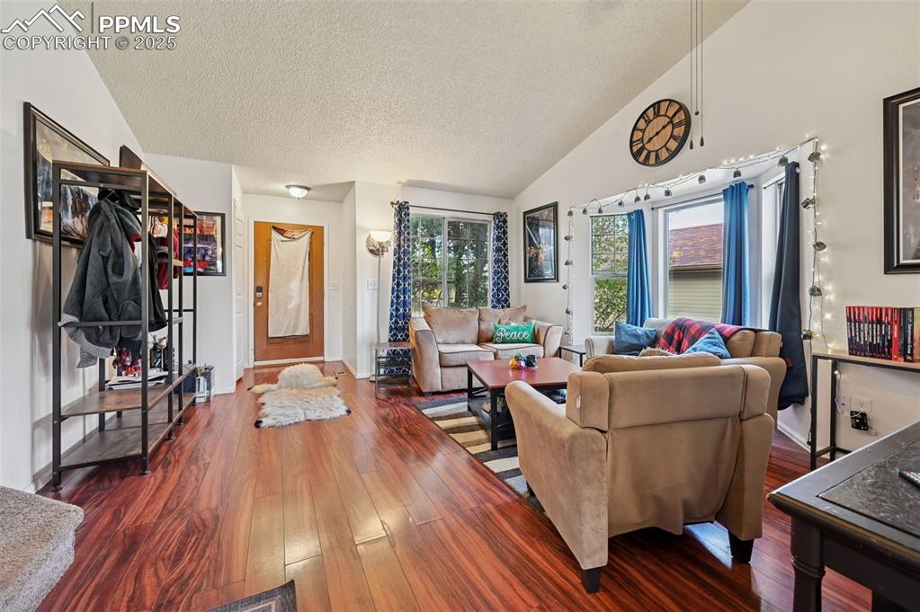 Image 4 of 27: Living room with dark wood-style flooring, a textured ceiling, and vaulted