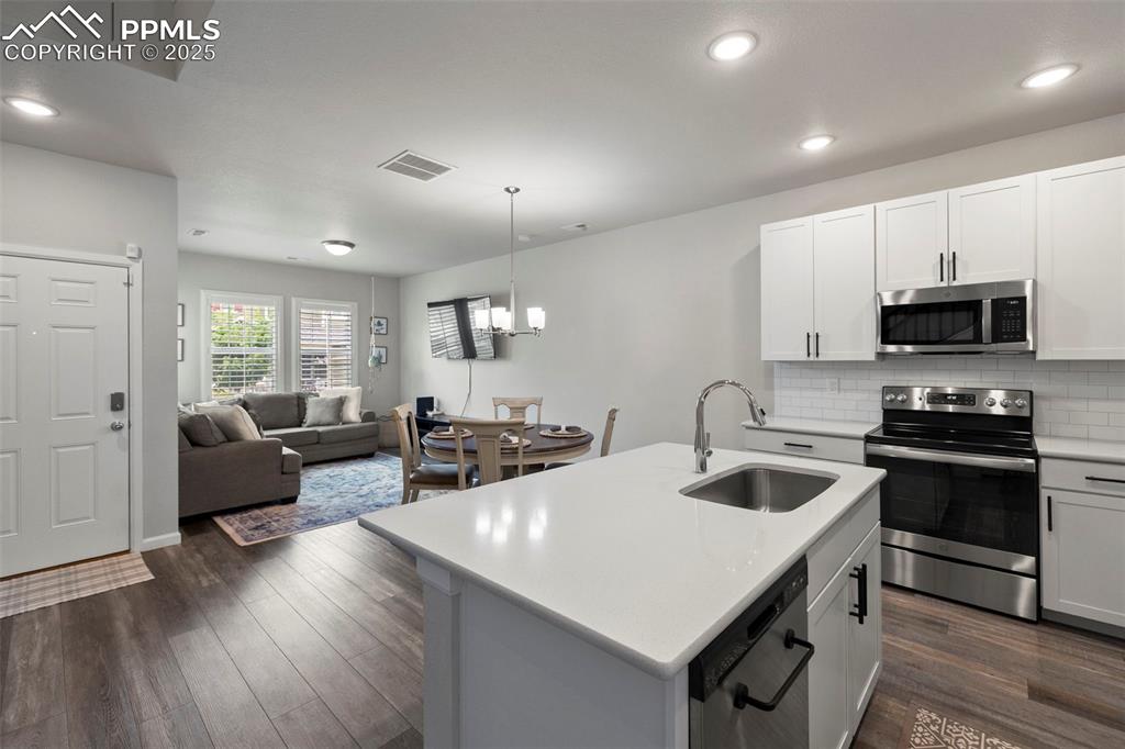 Image 11 of 24: Kitchen with stainless steel appliances, dark wood-style floors, light coun