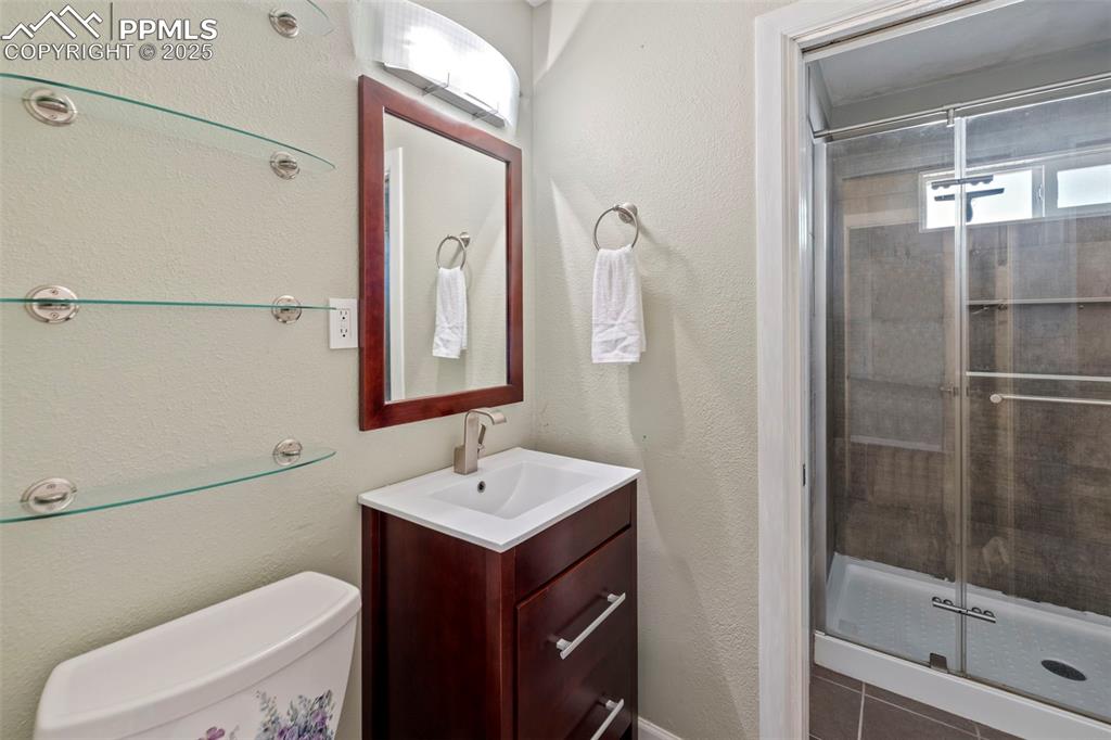 Image 15 of 30: Full bathroom featuring a stall shower, a textured wall, and vanity