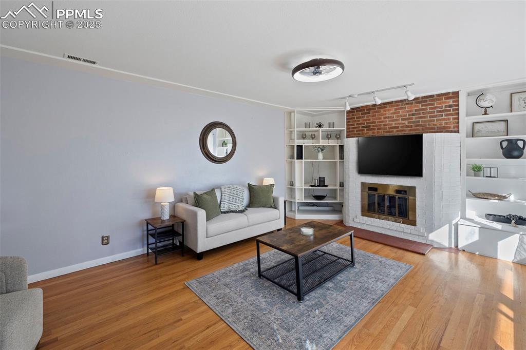 Image 3 of 30: Living area with track lighting, a brick fireplace, and light wood-style fl
