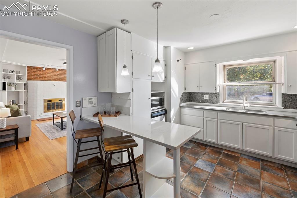 Image 5 of 30: Kitchen featuring white cabinets, a kitchen breakfast bar, decorative light