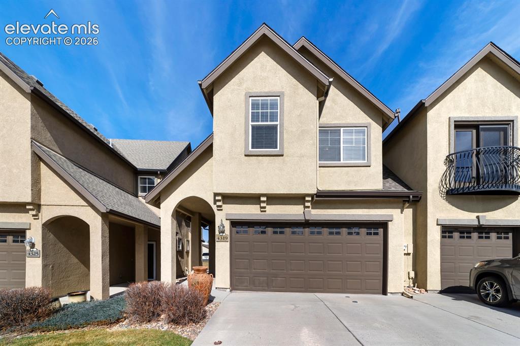 Caption: Stucco exterior featuring an arched entryway, gabled rooflines, a multi-section garage door with tra