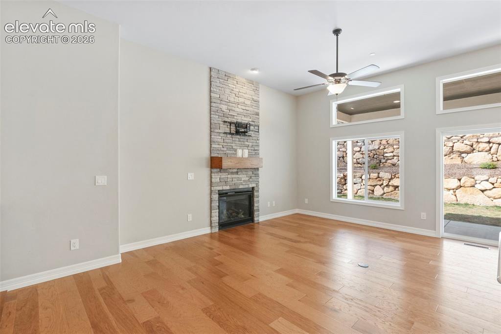 Image 10 of 47: Spacious living area featuring wood-finish flooring, a stone-clad fireplace