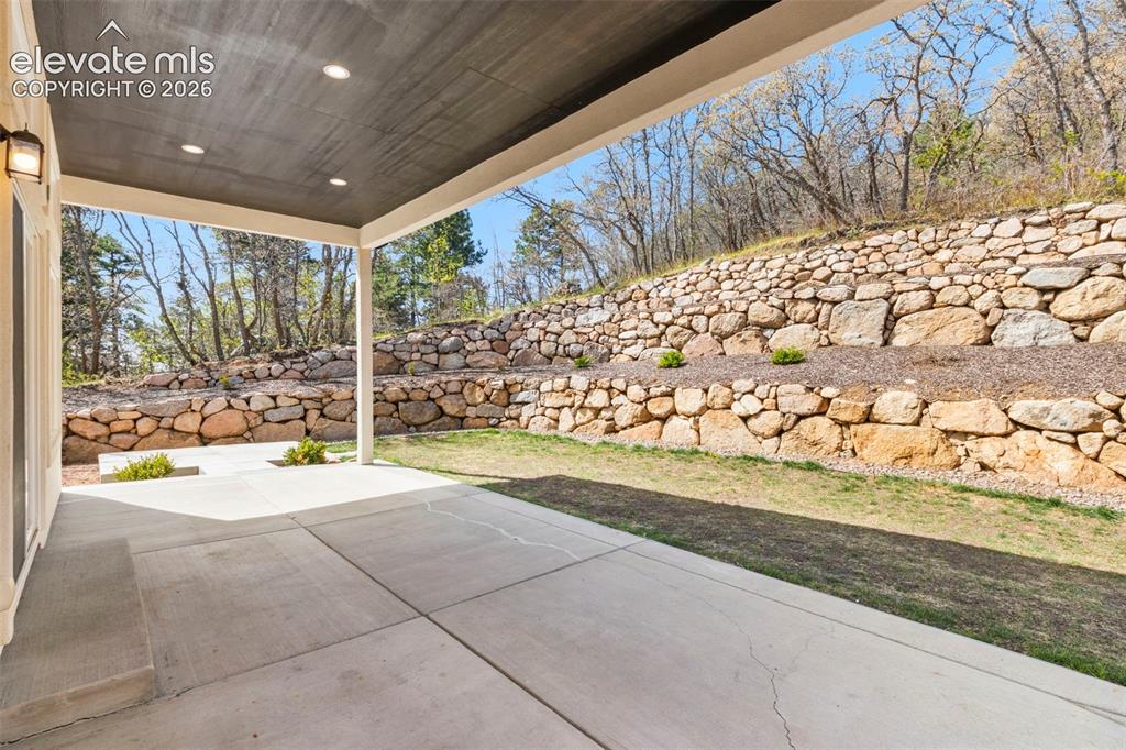 Image 41 of 47: Covered patio with recessed lighting, concrete flooring, and a stone retain