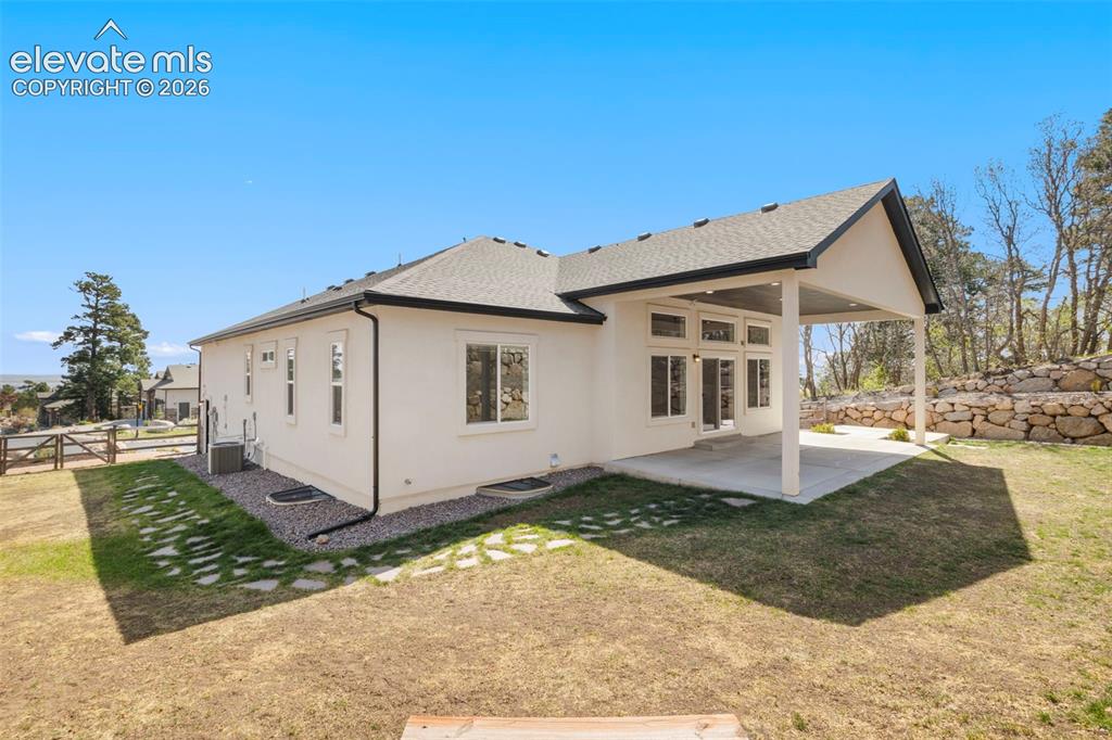Image 44 of 47: Rear exterior featuring a covered patio, multiple large windows, and a ston