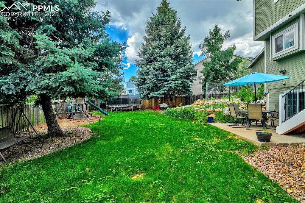 Image 30 of 32: Fenced backyard with a playground, a patio, and a trampoline