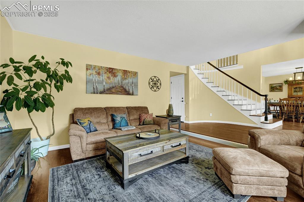 Image 4 of 32: Living room with stairs, wood finished floors, and a chandelier
