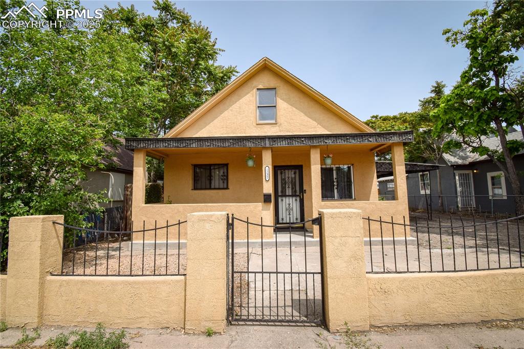 Caption: Bungalow-style home with a porch, stucco siding, and a fenced front yard