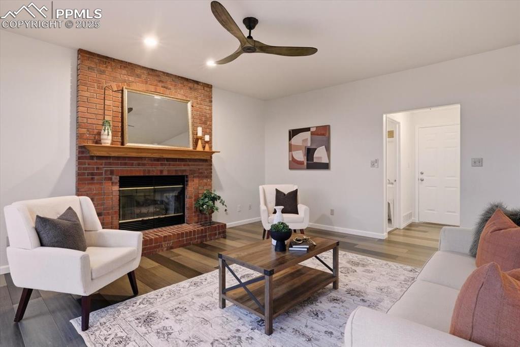 Image 12 of 31: Living area with wood finished floors, a brick fireplace, ceiling fan, and