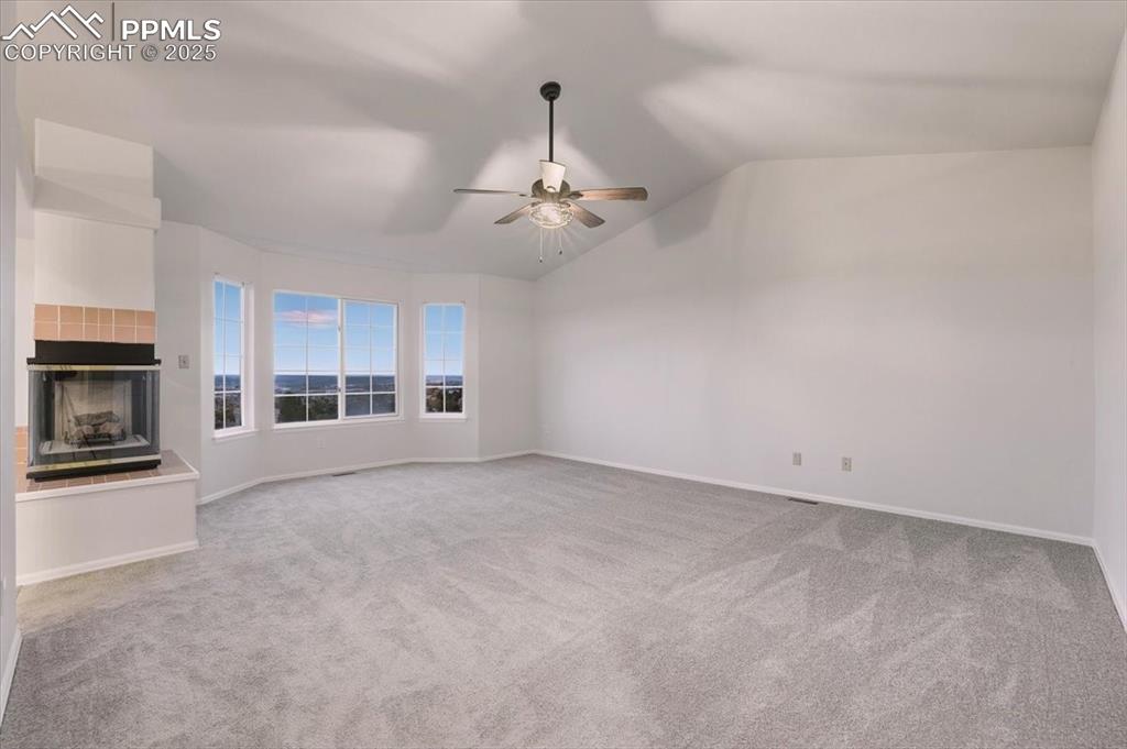Image 16 of 31: Unfurnished living room with light carpet, vaulted ceiling, a tiled firepla