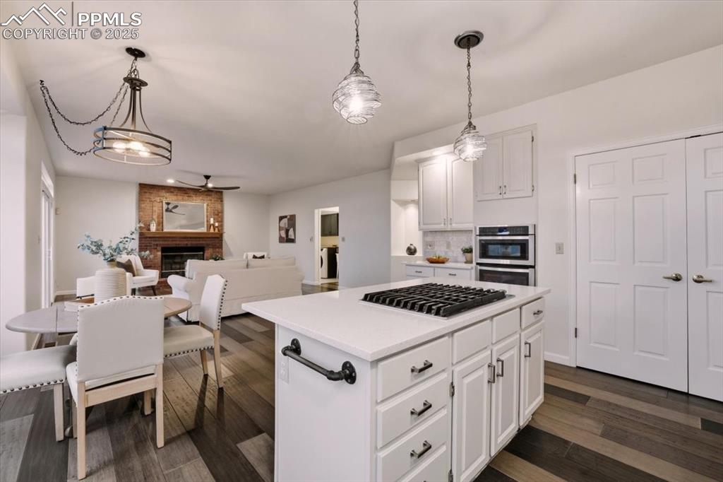 Image 8 of 31: Kitchen with a kitchen island, white cabinets, pendant lighting, a fireplac
