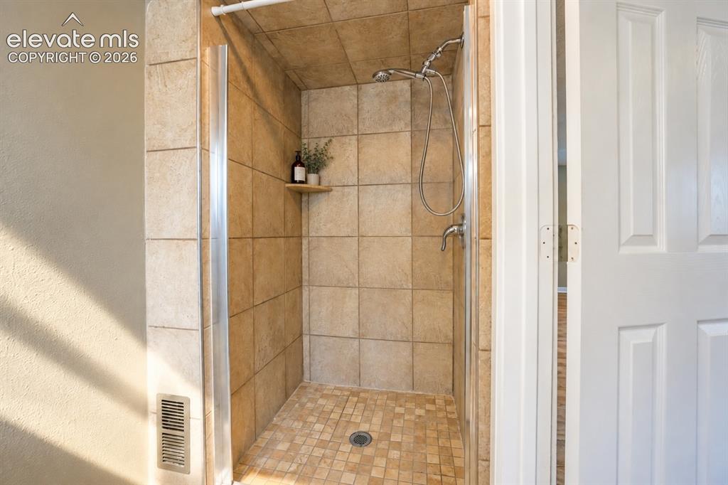 Image 25 of 29: Tiled shower with a built-in shelf, glass enclosure, and a handheld showerh