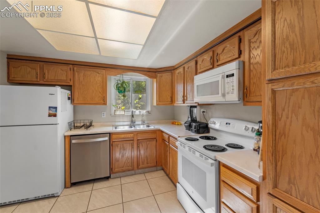 Image 18 of 38: Kitchen with white appliances, light countertops, brown cabinets, and light