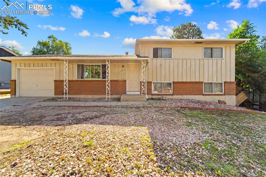 Image 9 of 38: Split level home with a garage, board and batten siding, driveway, and bric