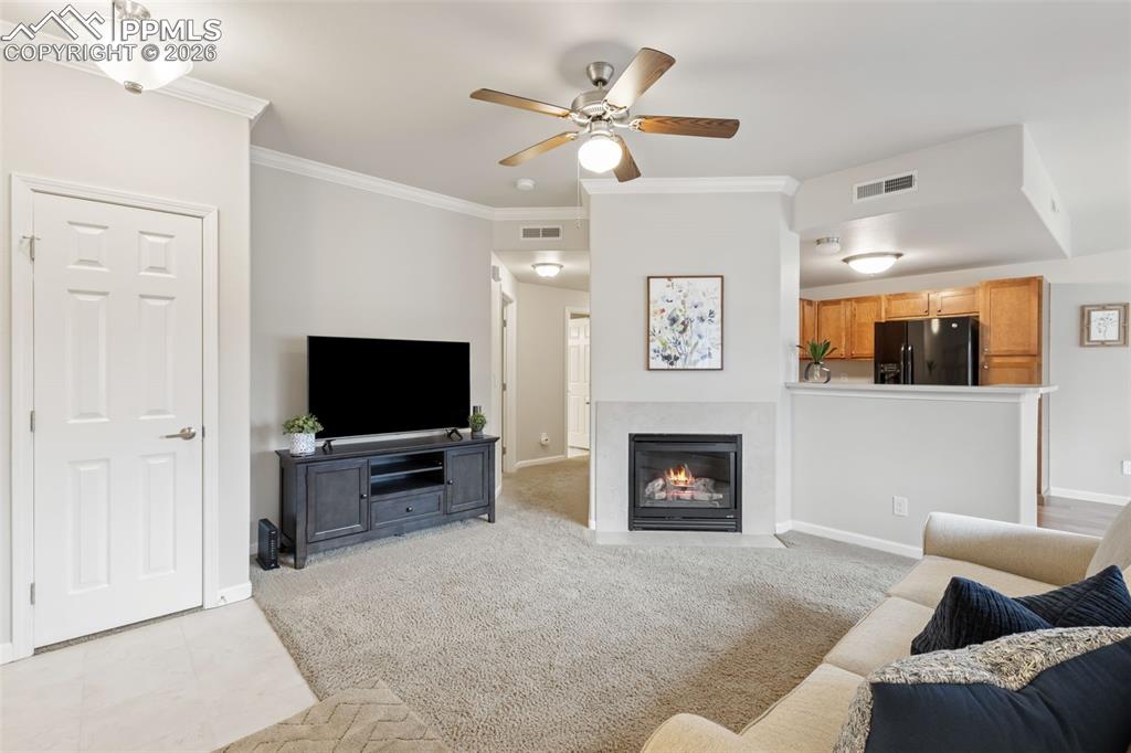 Image 5 of 26: Living area with crown molding, carpet, ceiling fan, and a fireplace with f