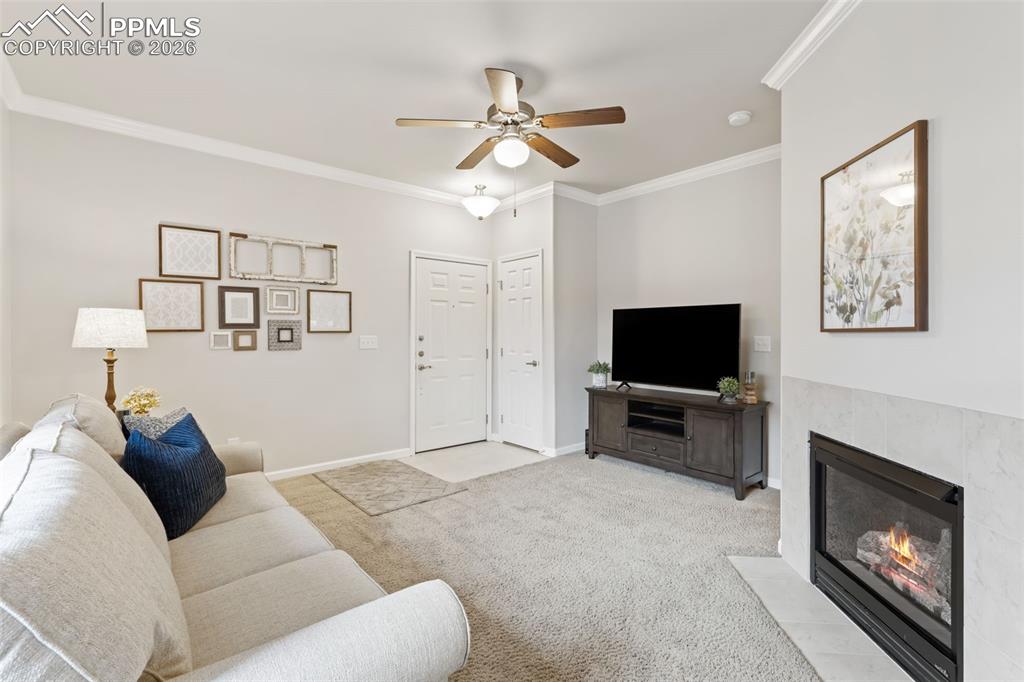 Image 6 of 26: Living area with crown molding, carpet, ceiling fan, and a fireplace with f