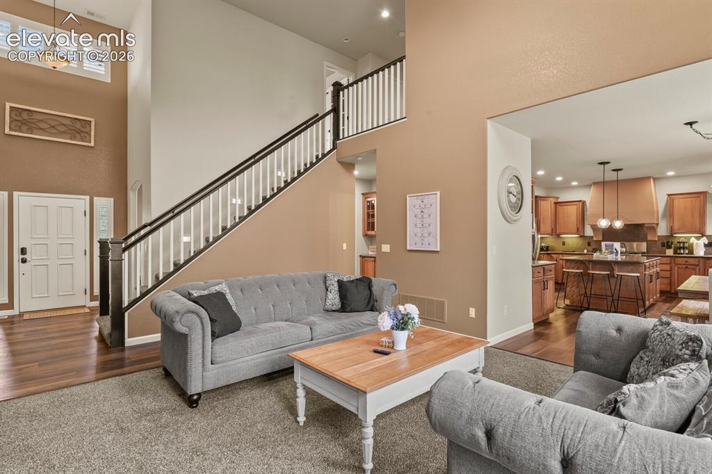 Image 12 of 47: Spacious living area featuring high ceilings, a prominent staircase with wh