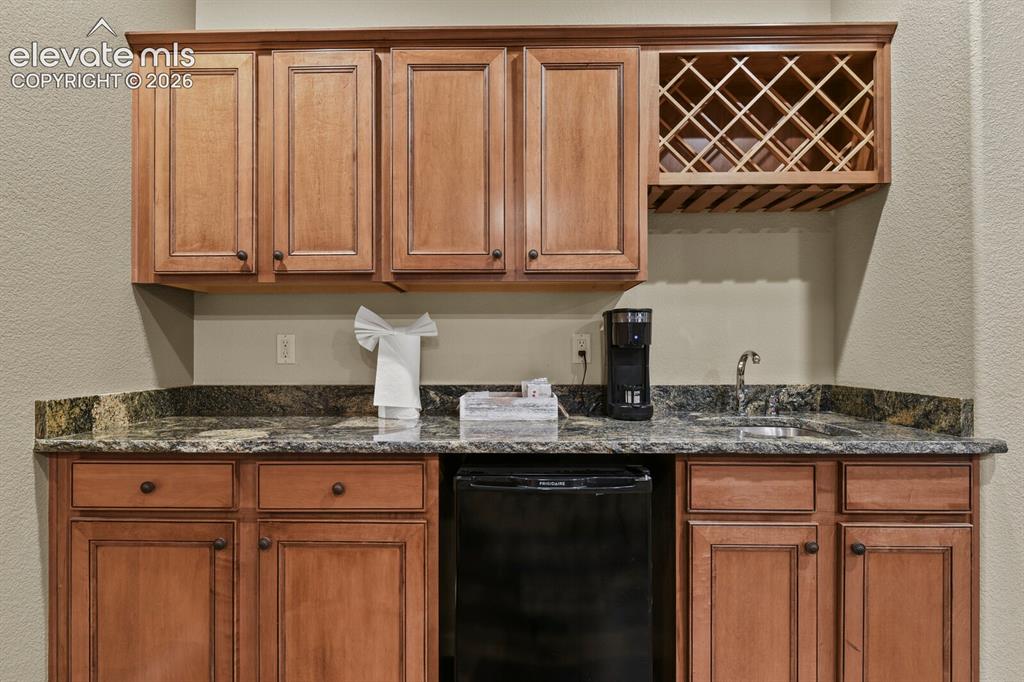 Image 39 of 47: Built-in wet bar featuring wood cabinetry, a bottle rack, a compact refrige