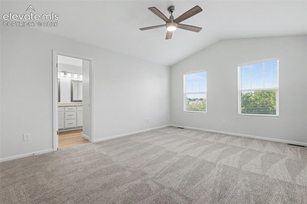 Image 20 of 27: Spacious primary bedroom featuring vaulted ceiling with a ceiling fan and