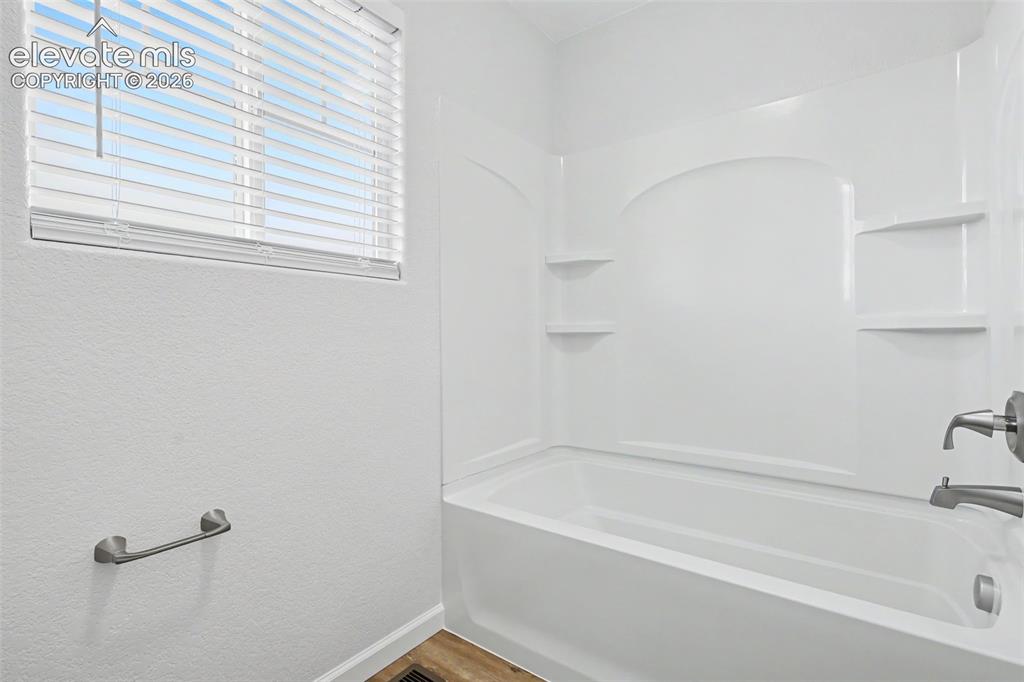 Image 22 of 27: Bathtub and shower combination featuring a white surround with integrated s