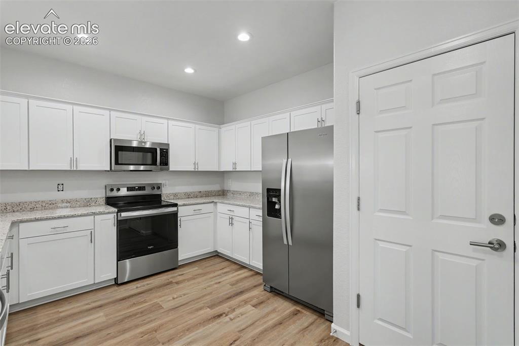 Image 7 of 27: Modern kitchen featuring white shaker cabinetry, granite countertops, stain