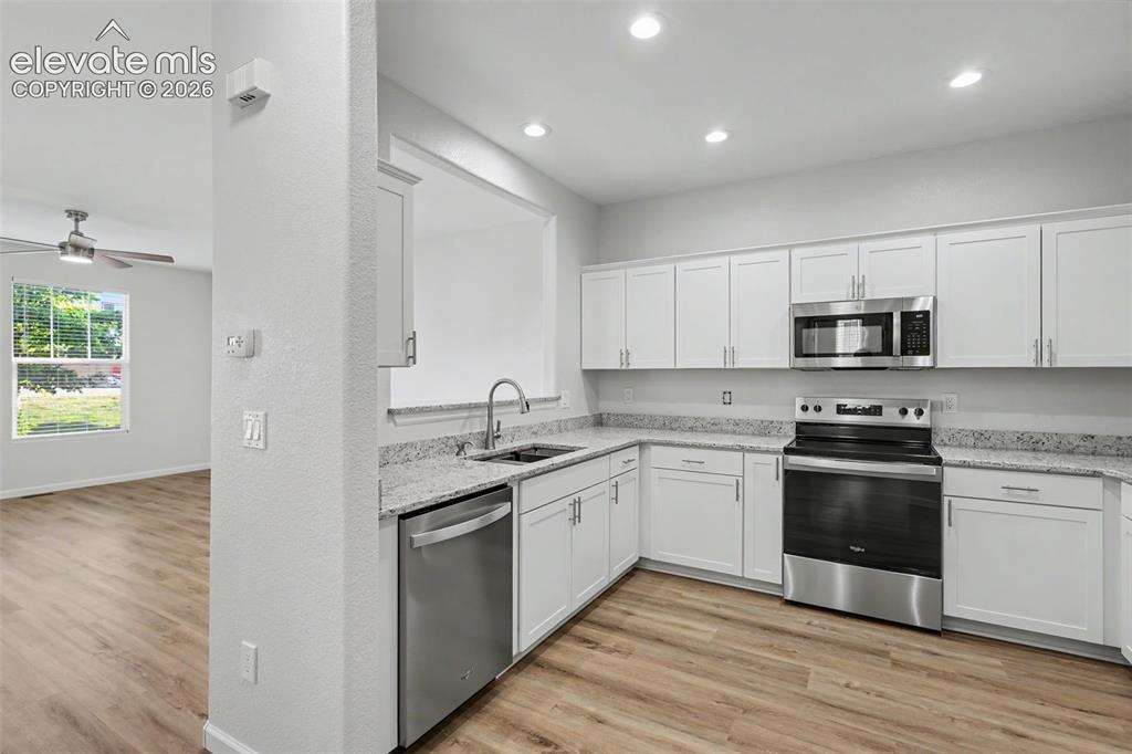 Image 8 of 27: Modern kitchen featuring white shaker cabinetry, granite countertops, stain
