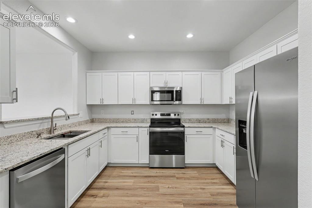 Image 9 of 27: Modern kitchen featuring white shaker cabinetry, granite countertops, stain