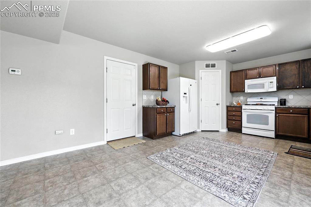 Image 11 of 46: Kitchen with white appliances, dark brown cabinets, and backsplash