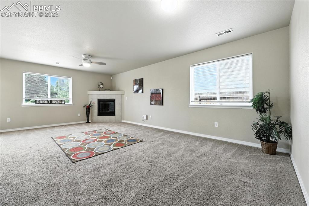 Image 14 of 46: Unfurnished living room with ceiling fan, carpet flooring, and a tile firep