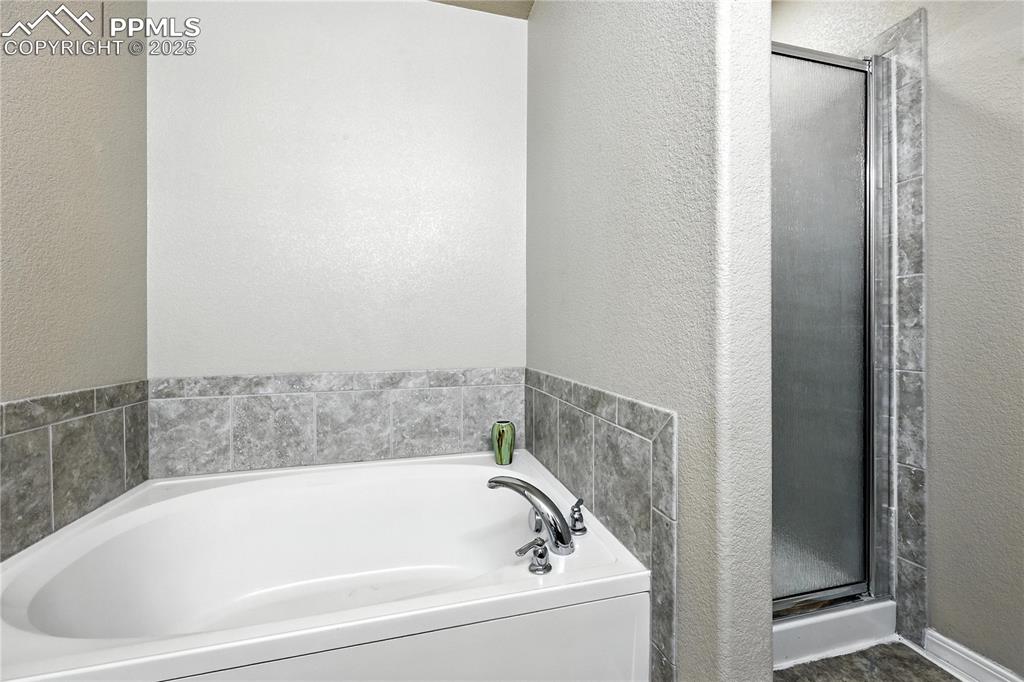 Image 22 of 46: Full bathroom with a textured wall, a bath, and a stall shower