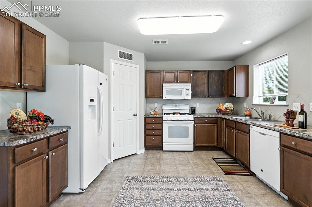 Image 7 of 46: Kitchen featuring white appliances, tasteful backsplash, and dark counterto