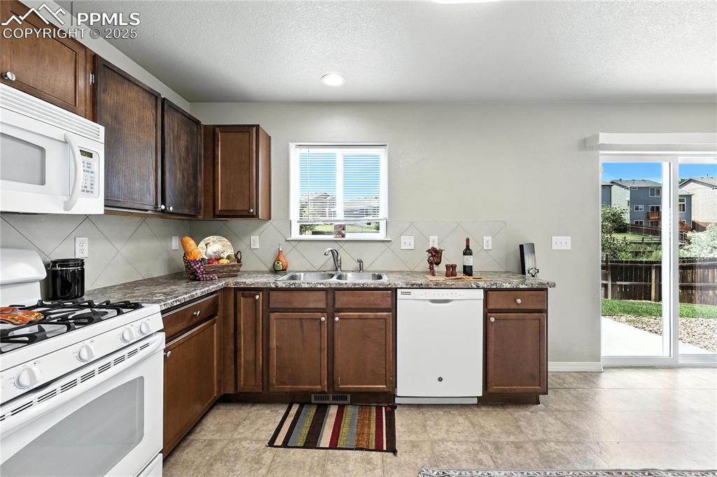 Image 9 of 46: Kitchen featuring white appliances, backsplash, a textured ceiling, and dar
